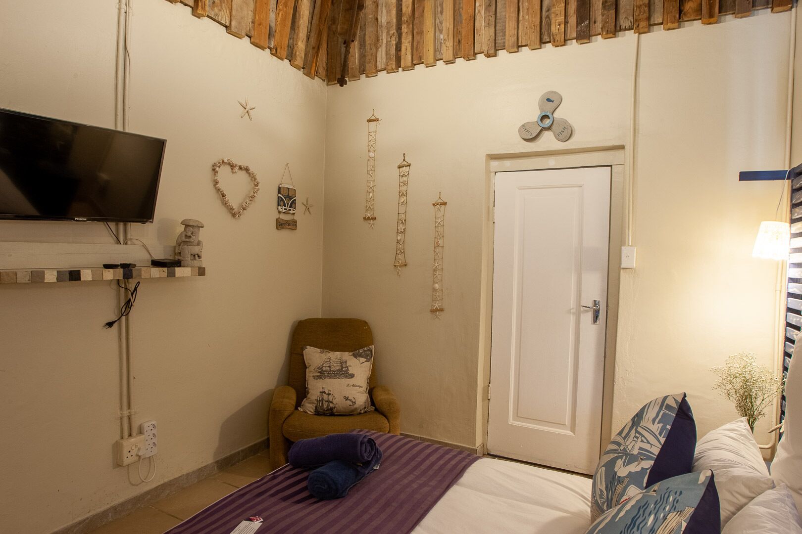 Un dormitorio con cama, una silla, un televisor y diferentes adornos en las paredes.