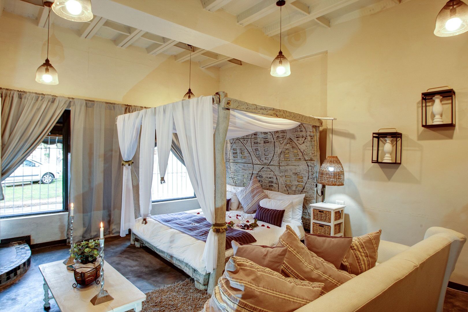 Un dormitorio con cama con dosel, un sofá, una mesita con una planta y una ventana con cortinas.