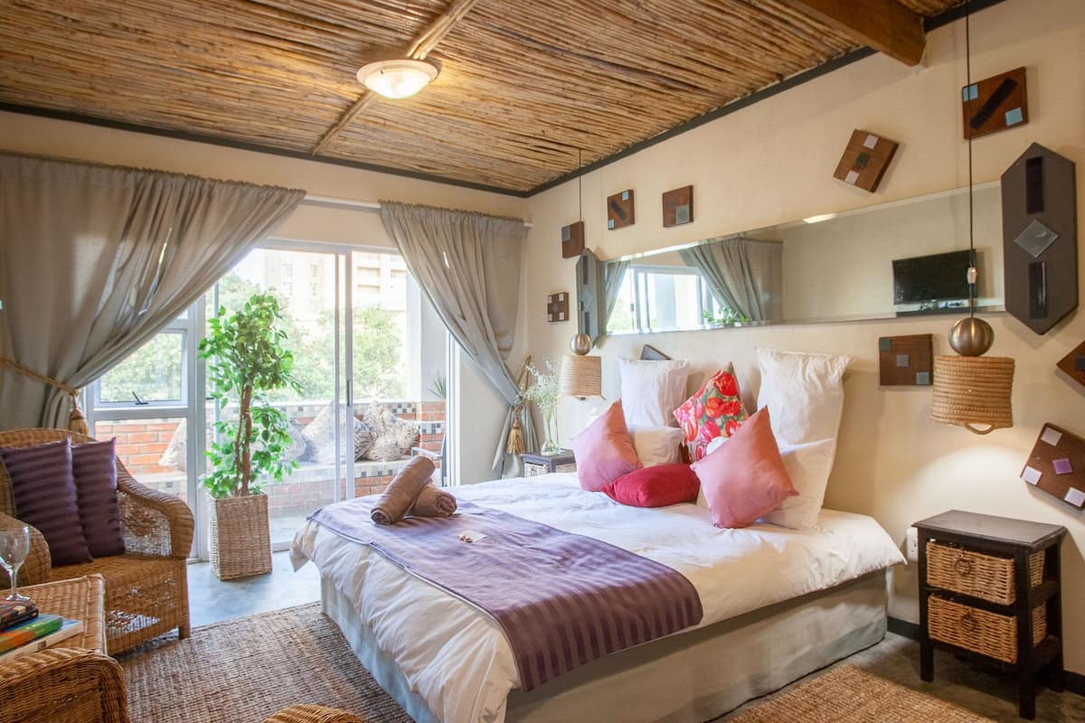 Ein Schlafzimmer mit einem großen Bett, einem Korbstuhl, einem Nachttisch und Blick ins Freie.