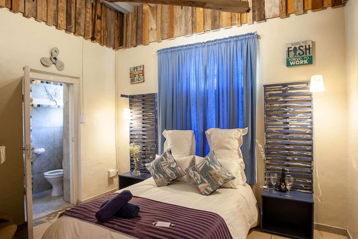 Ein Schlafzimmer mit einem Bett, einem Nachttisch, einer Lampe und einem Fenster mit blauen Vorhängen.