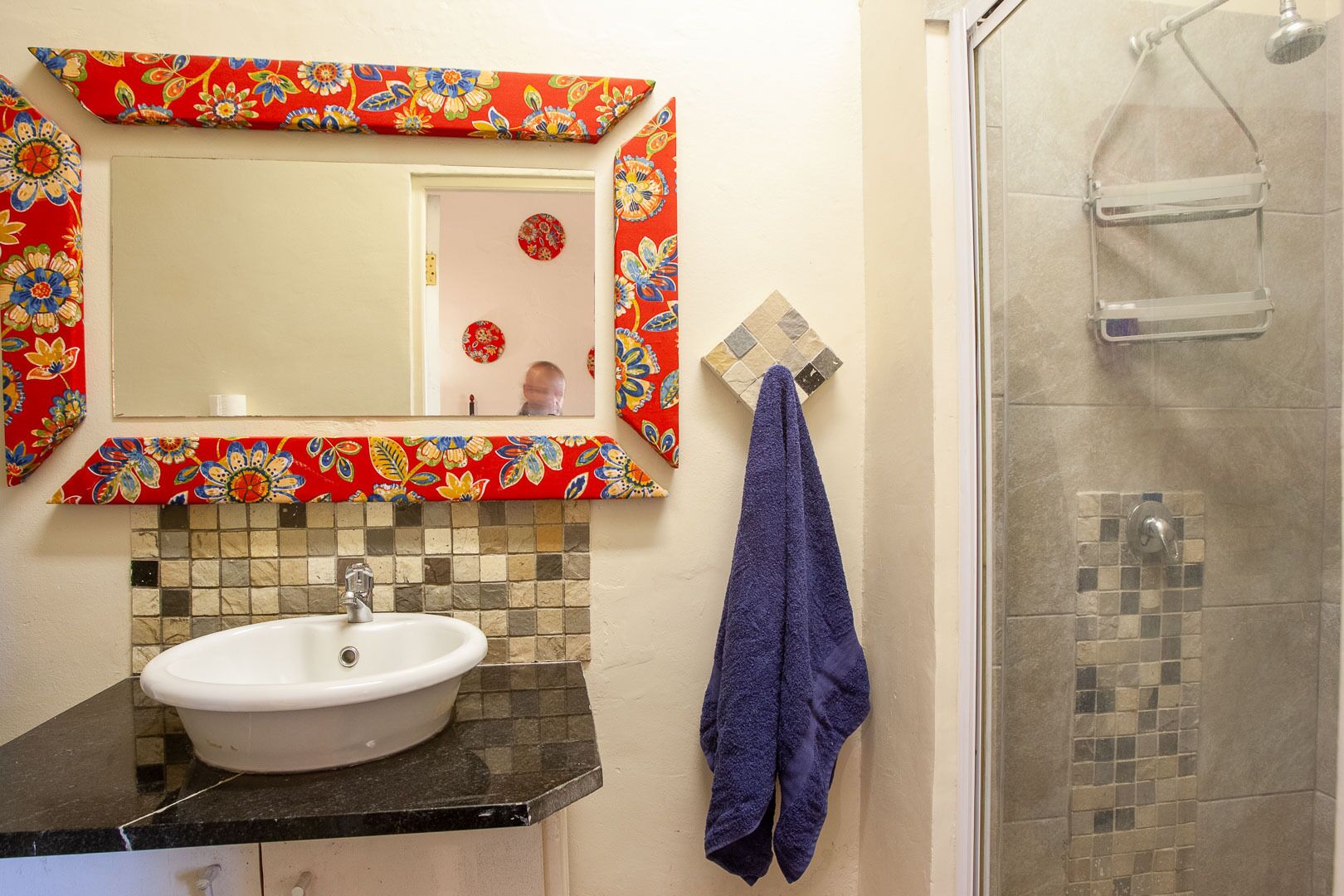 Un bagno con un lavandino bianco, uno specchio con cornice floreale e una doccia.