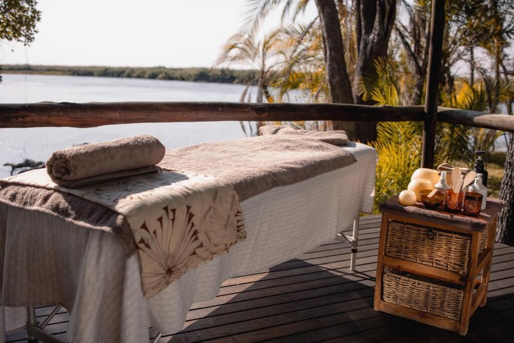A massage table set up on a wooden deck with a view of a lake and palm trees.