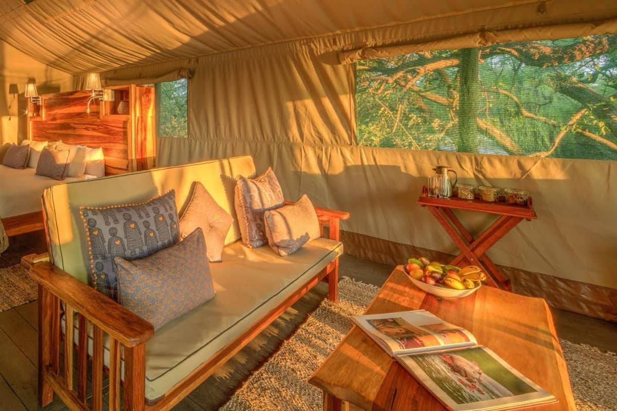 A tented accommodation with two beds, a sofa, and a dining area.