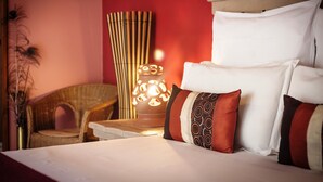 Un lit bien fait, agrémenté d’oreillers blancs et à motifs, une chaise en osier et une lampe décorative dans une pièce aux murs rouges.