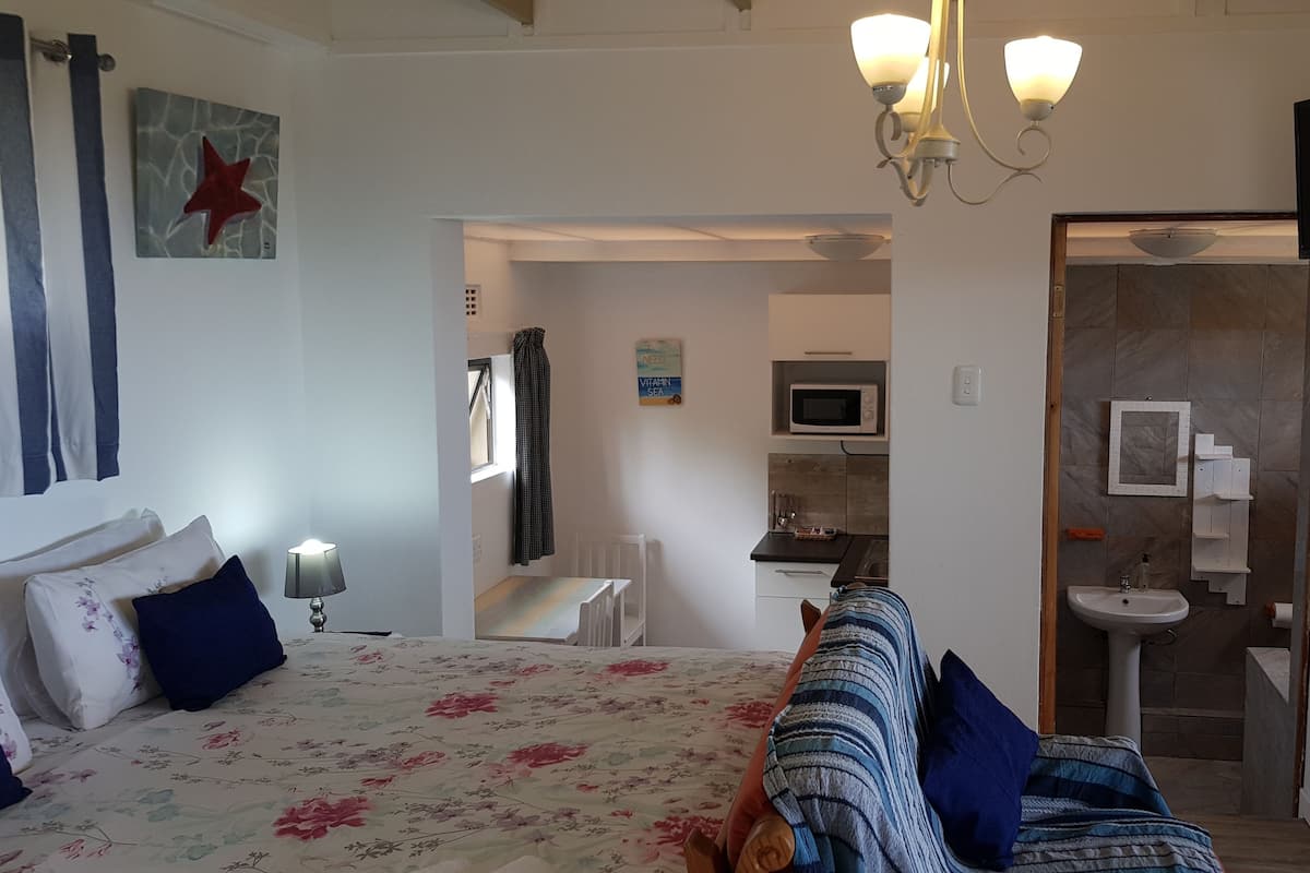 A bedroom with a bed, a bedside table, a lamp, a TV, and a bathroom visible through an open door.