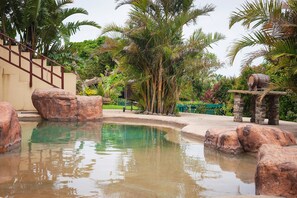 A pool with large rocks, palm trees, and a wooden bridge. - Hoylake Inn (East London)