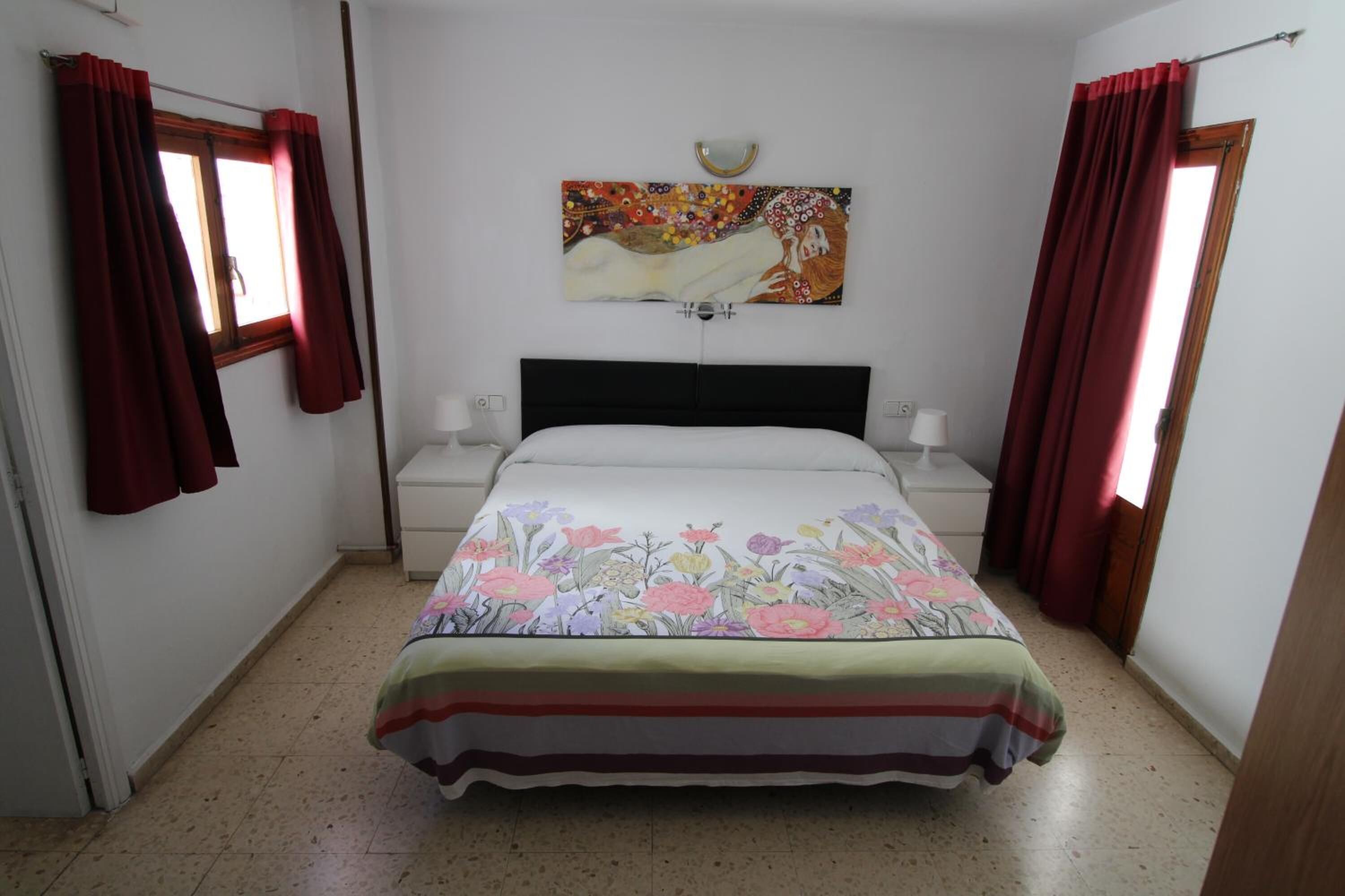 A bedroom with a bed, nightstands, a wall-mounted lamp, and a painting.