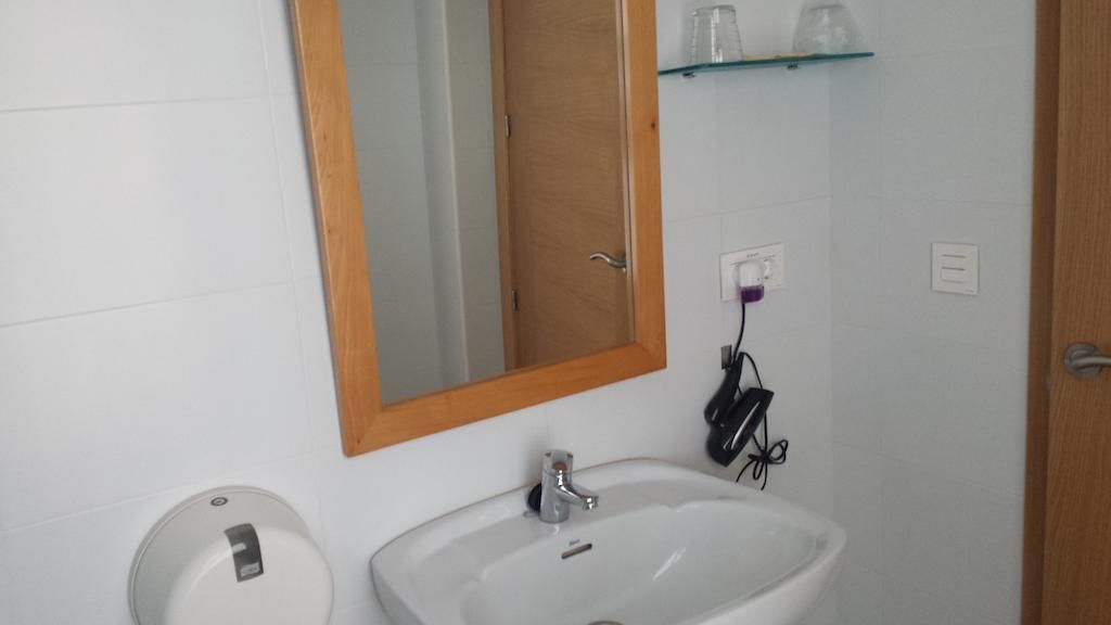 Casa de banho com lavatório branco, espelho e prateleira de vidro acima do lavatório.