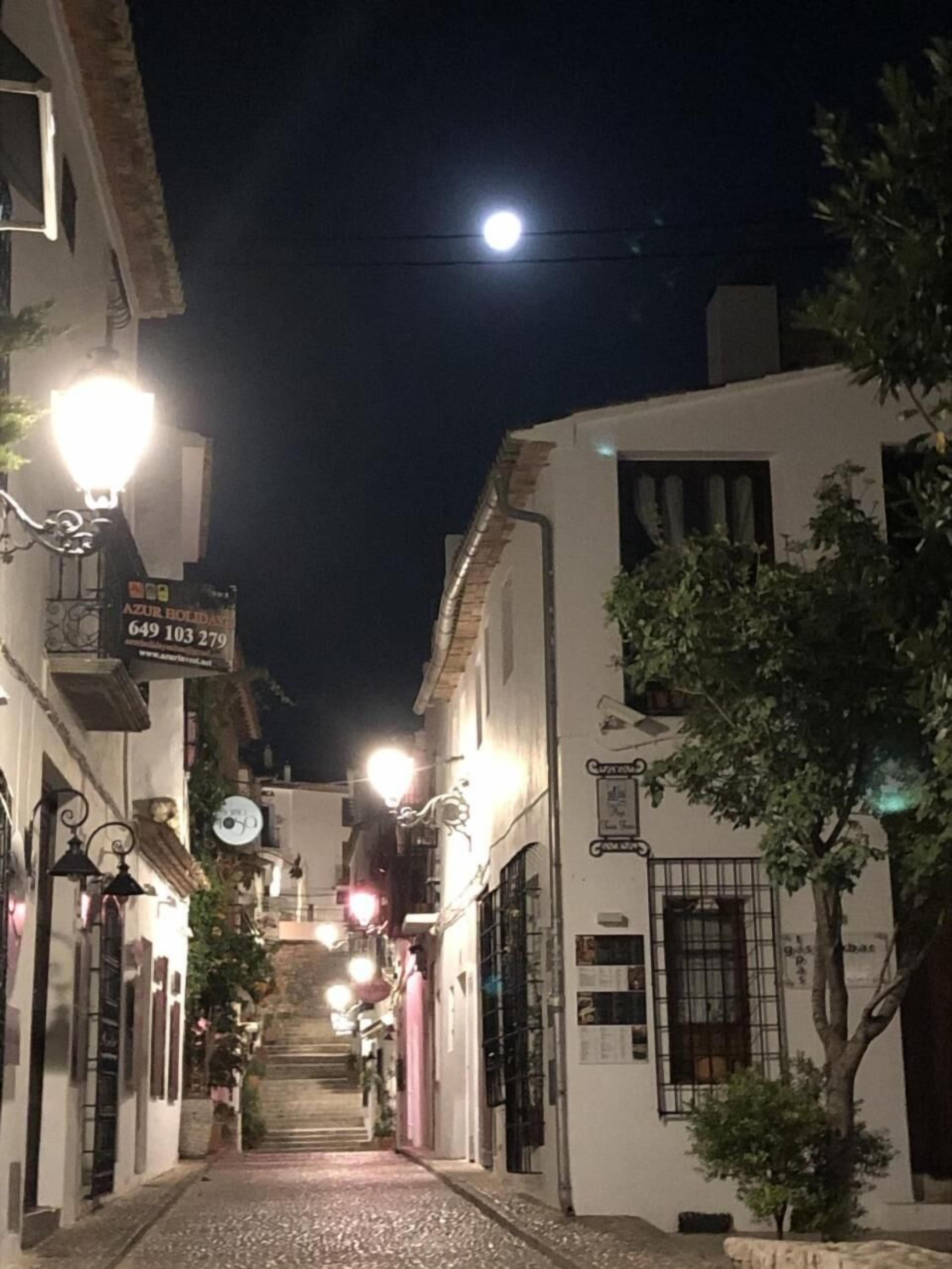 Una calle estrecha flanqueada por edificios, iluminada por farolas.