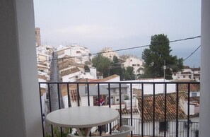 Un balcón con una mesa redonda y sillas, con vistas a una zona residencial con edificios blancos y una torre de iglesia.