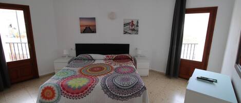 A bedroom with a bed, nightstands, a dresser, and two windows with curtains.