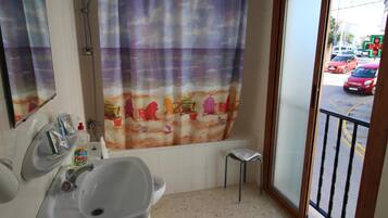 A bathroom with a shower, a sink, a toilet, and a window with a view of the street.