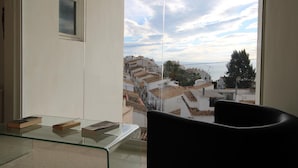 A balcony with a glass table, a black chair, and a view of a cityscape with terraced buildings.