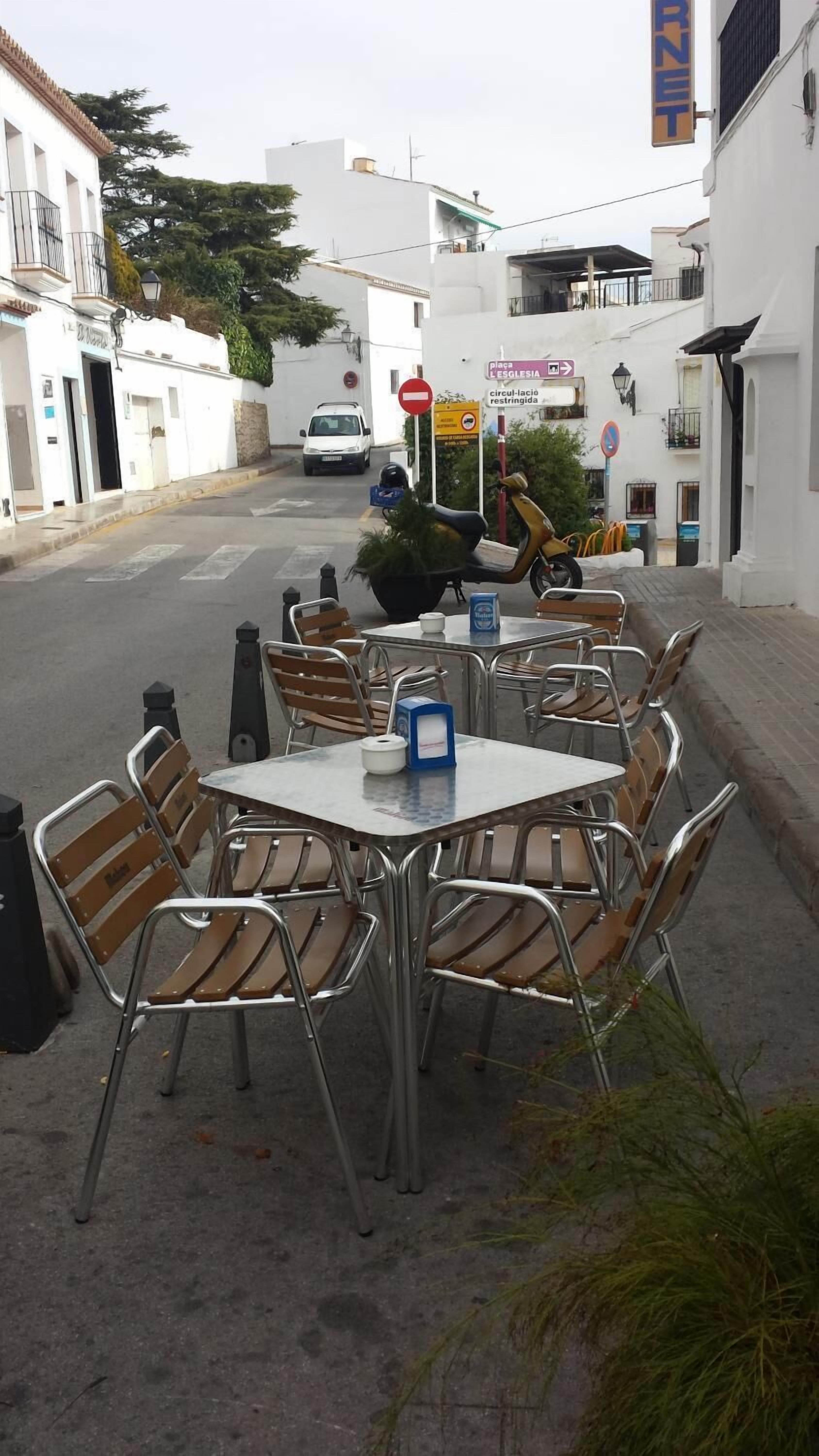 Un área de estar al aire libre con mesas y sillas de metal, un enfriador azul y un letrero que dice 'place L'EGLISESIA'.