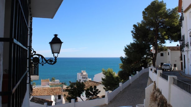 A coastal street with buildings, a lamp post, and a view of the sea.