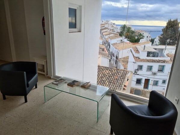 Una sala de estar moderna con una mesa de centro de vidrio, dos sillones negros y vistas a un pueblo costero.