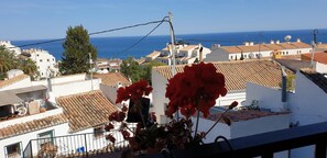 Un pueblo costero con edificios de tejados de terracota, un cielo azul claro y vista al mar.