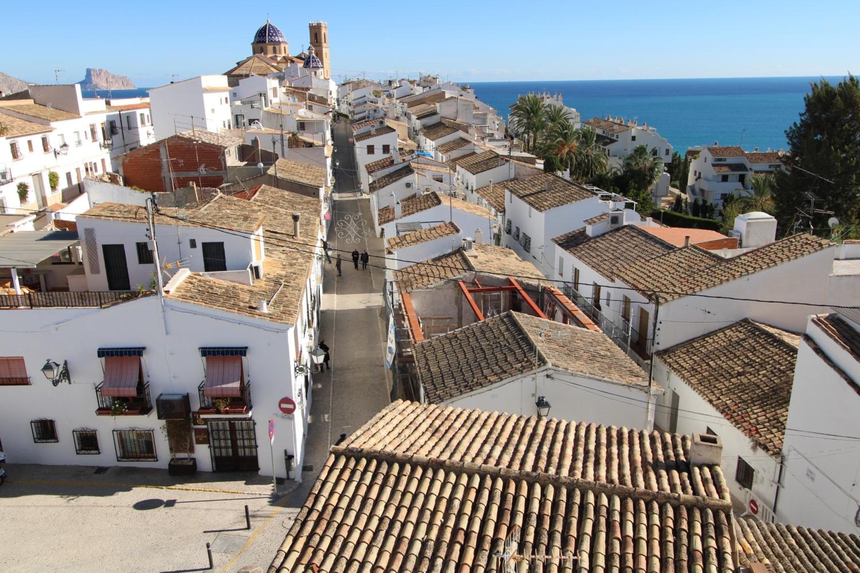 Un pueblo costero con edificios blancos, tejados de tejas rojas y vistas despejadas al mar.