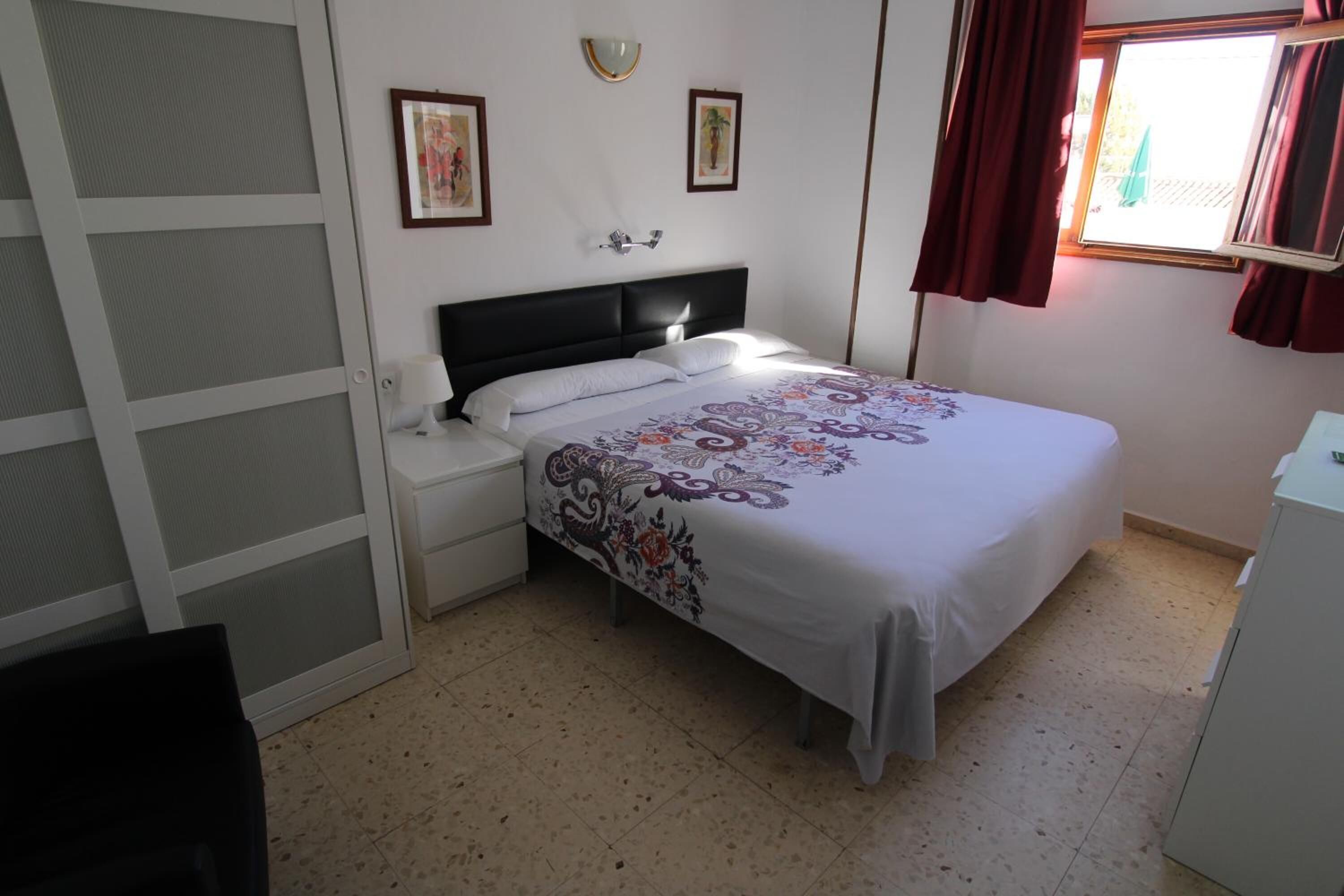 A bedroom with a bed, nightstand, and a window with curtains.