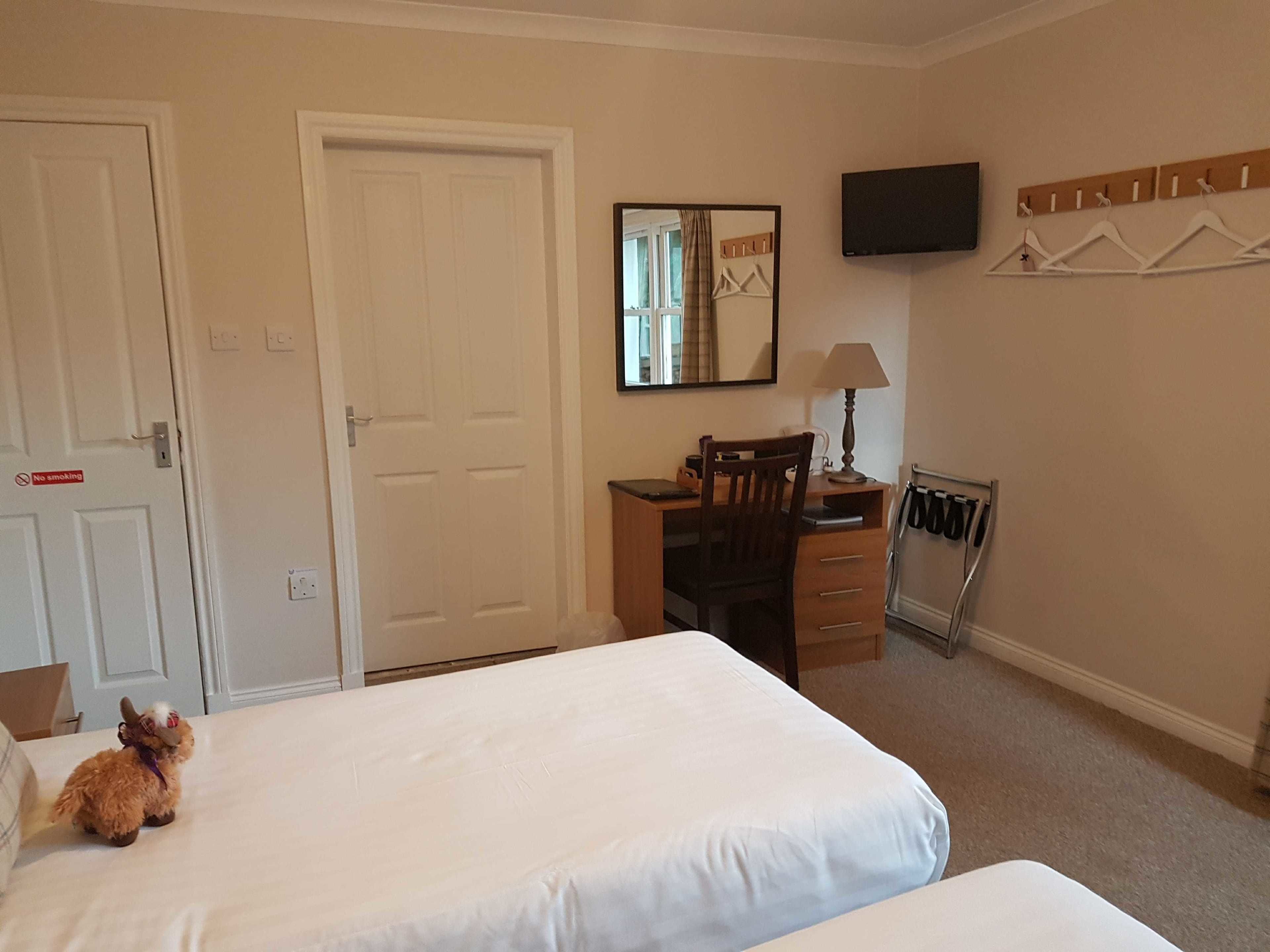 A hotel room with two beds, a desk with a chair, a TV mounted on the wall, and a coat rack.
