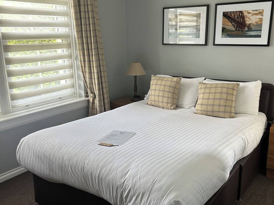 A neatly made bed with a pillow, a bedside lamp, and two framed pictures on the wall.