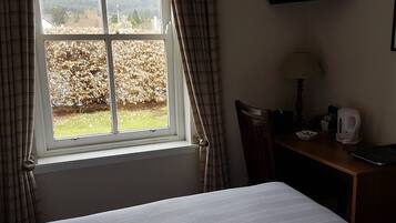 A hotel room with a bed, a desk with a lamp, a television on the wall, and a window with curtains.