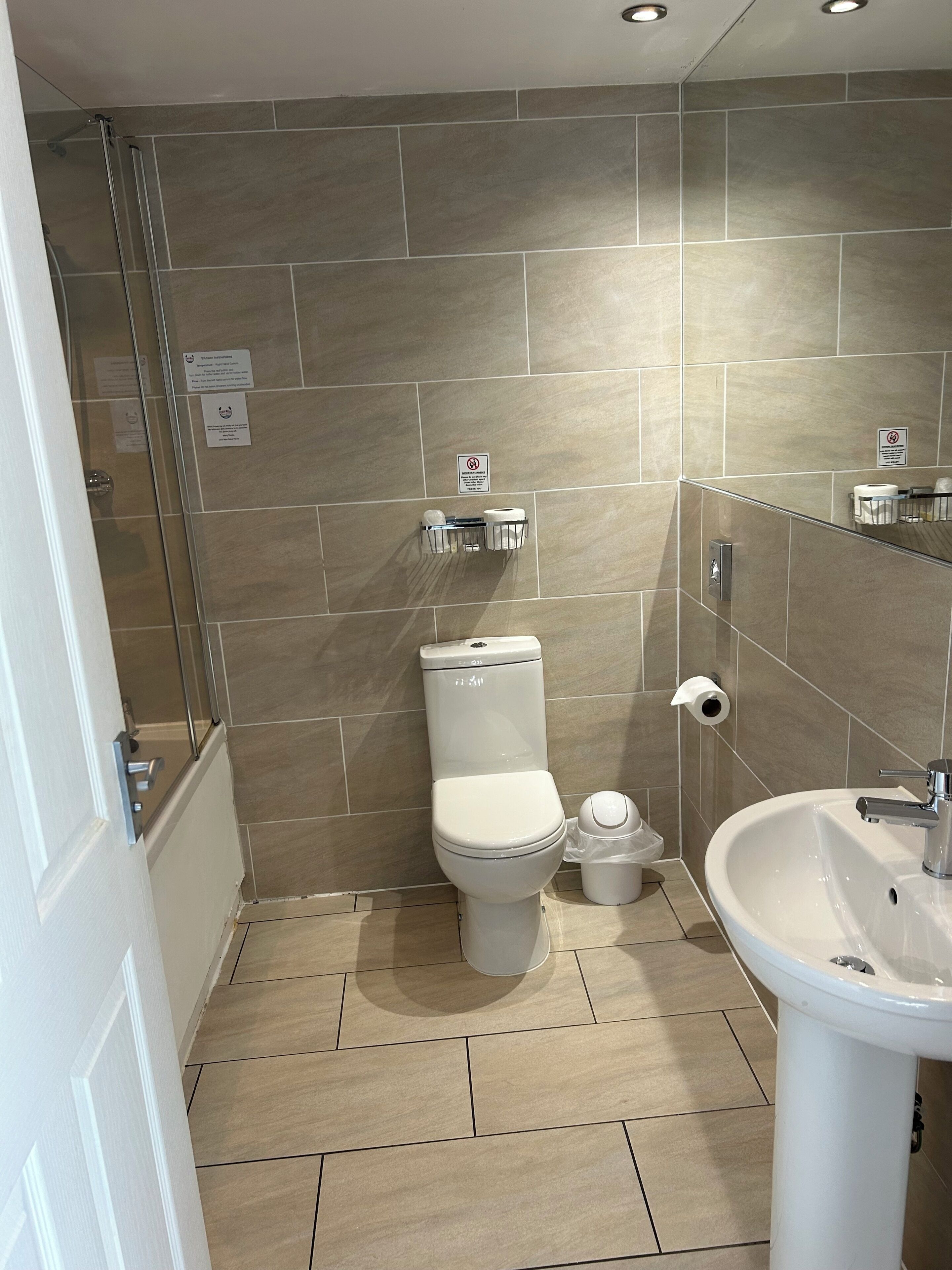 Een badkamer met toilet, bidet, wastafel, betegelde wanden en een douchehoek.