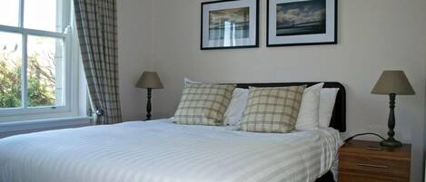 A neatly made bed with a white duvet, two bedside lamps, a wooden nightstand with drawers, and two framed pictures on the wall.