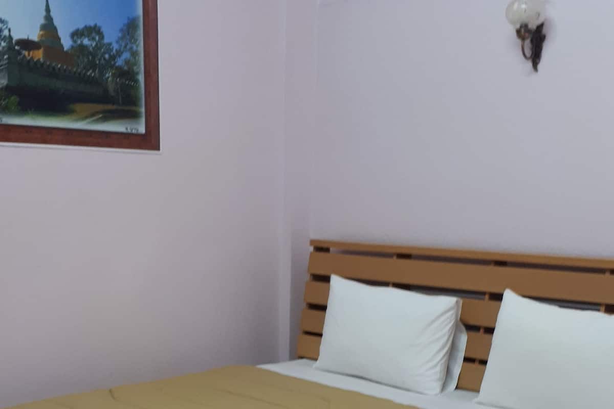 A neatly made bed with a brown bedspread and two white pillows, a framed picture on the wall, and a small decorative item on the nightstand.