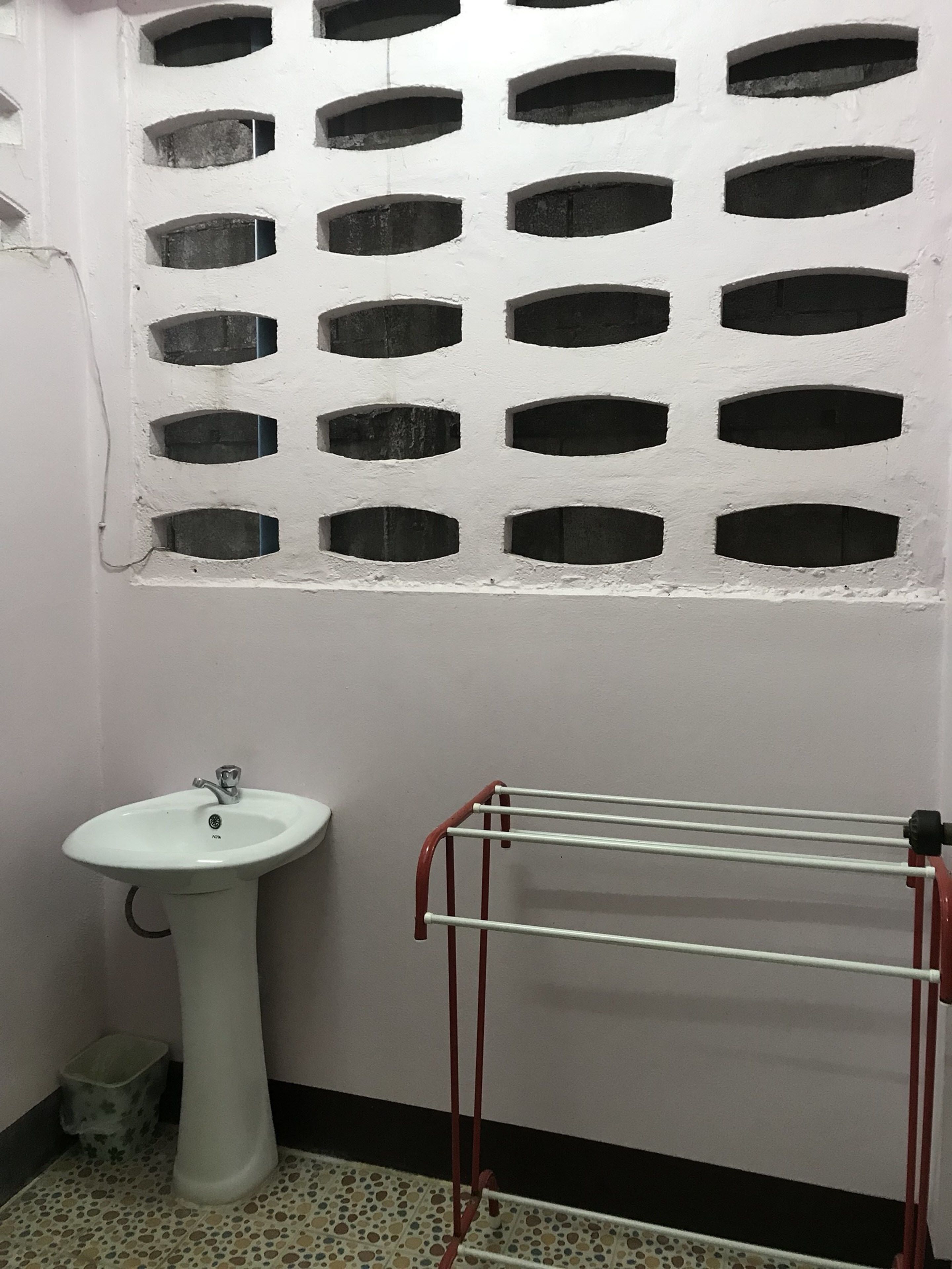 Ein Badezimmer mit einem Standwaschbecken, einem Handtuchhalter und einem Fenster mit Gitterverglasung.