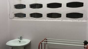 Ein Badezimmer mit einem Standwaschbecken, einem Handtuchhalter und einem Fenster mit Gitterverglasung.