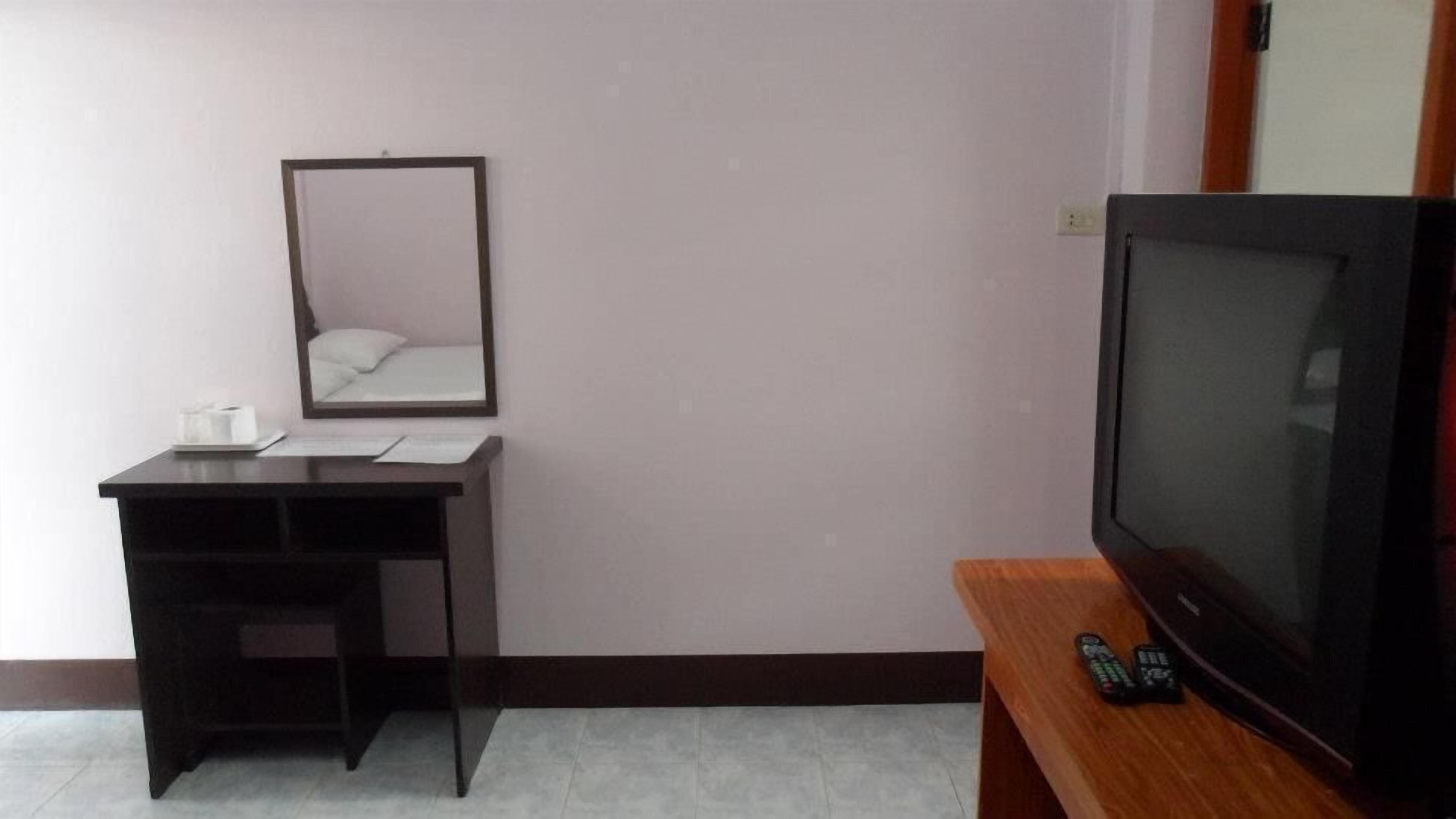 A small room with a desk, a mirror, a television, and a remote control.