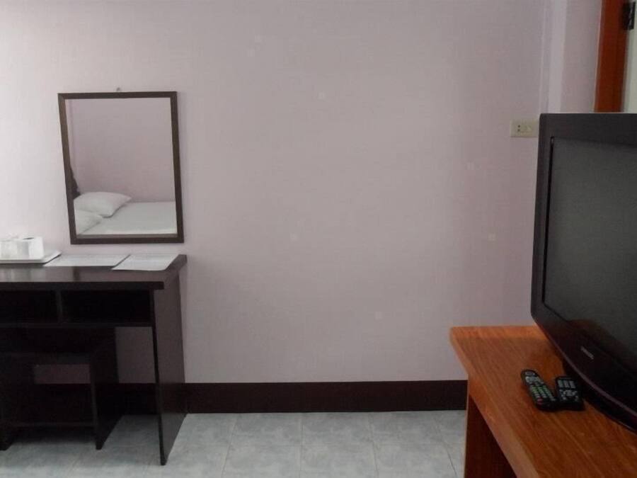 A small room with a desk, a mirror, a television, and a remote control.