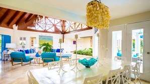 A spacious living area with a dining table, blue chairs, and a chandelier. - Unlimited Luxury Laureanne's Villa (La Romana)