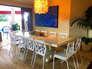 A dining area with a long table, white chairs, and a decorative hanging light fixture.