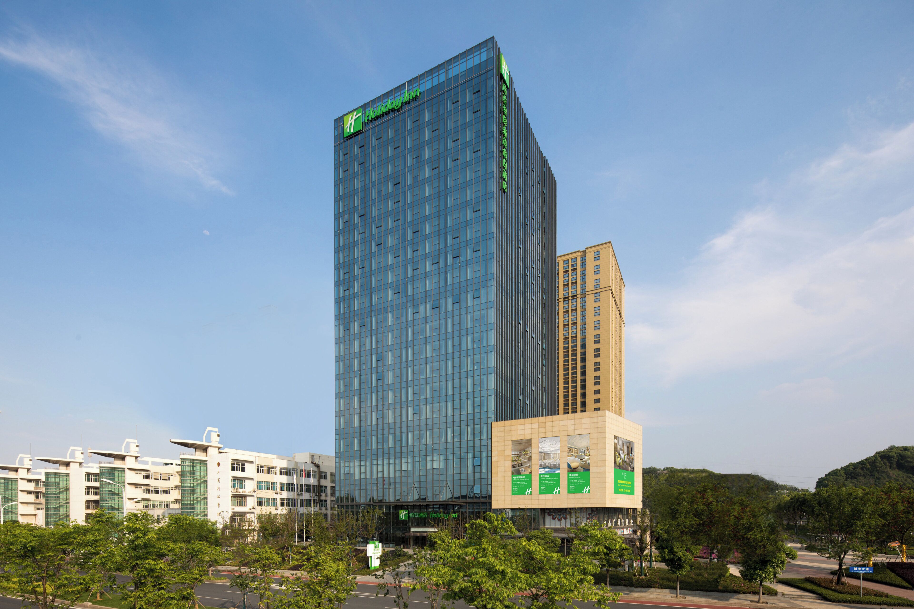 A modern high-rise hotel with a prominent glass facade and a green logo at the top.