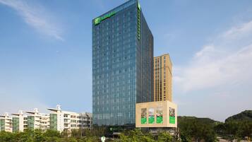 A modern high-rise hotel with a prominent glass facade and a green logo at the top.