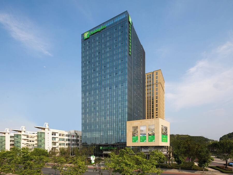 A modern high-rise hotel with a prominent glass facade and a green logo at the top.