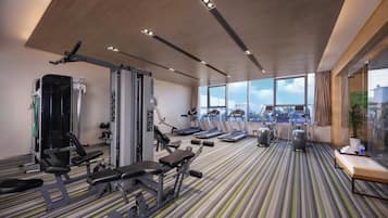 A modern gym with various exercise equipment, large windows, and a striped floor.