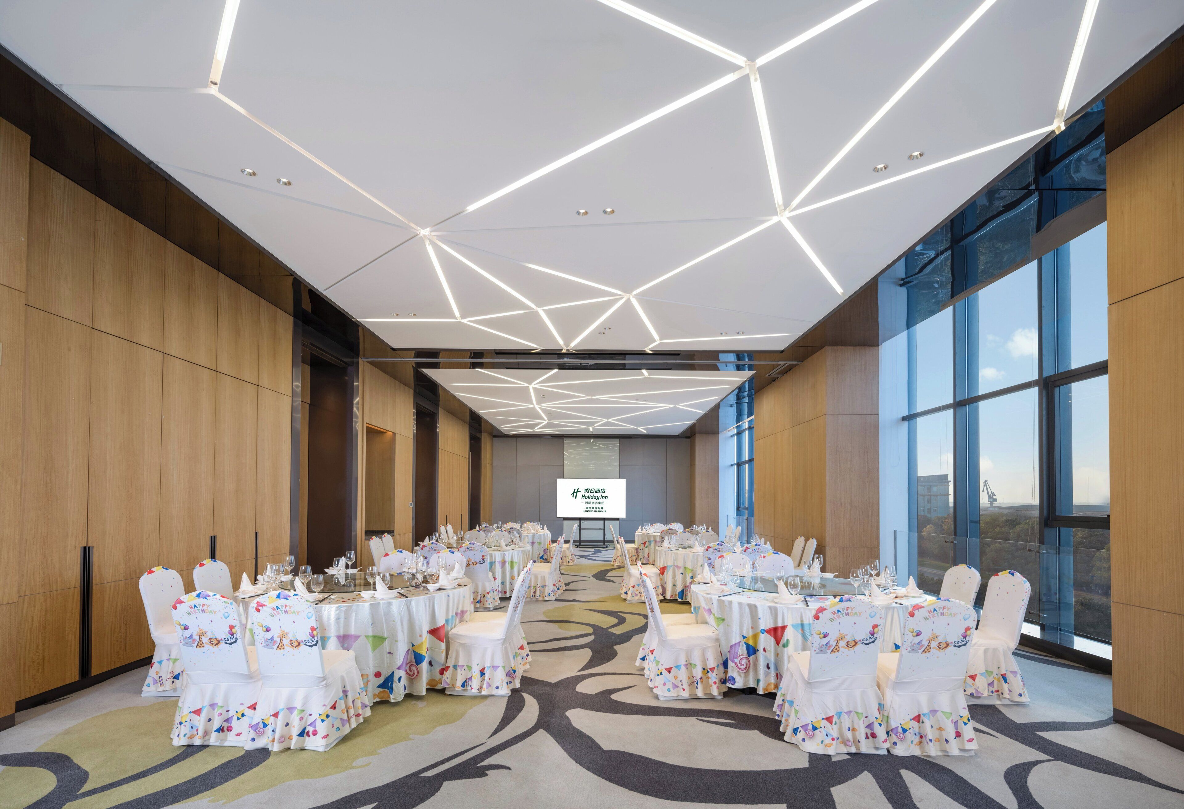 A banquet hall with round tables, white chairs, and a large screen at the front.