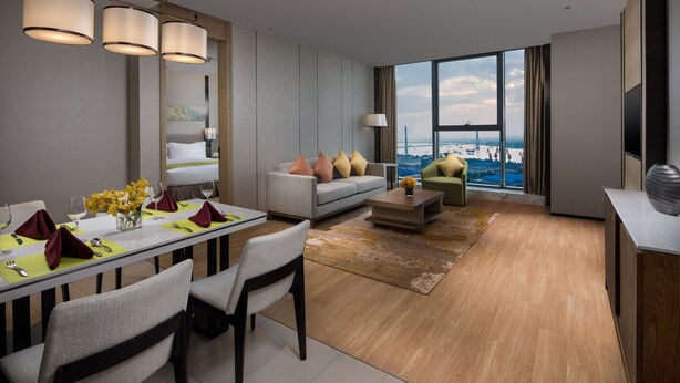 A modern hotel room with a dining area, a sofa set, a coffee table, and a large window with a city view. - Holiday Inn Nanjing Harbour by IHG (Nanjing)