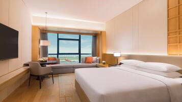 A hotel room with a large bed, a desk with a chair, a television, and a view of an airport.