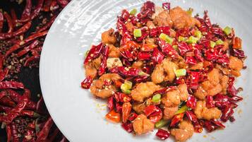 A white plate with a dish of fried chicken pieces, garnished with red chili peppers and green onions.
