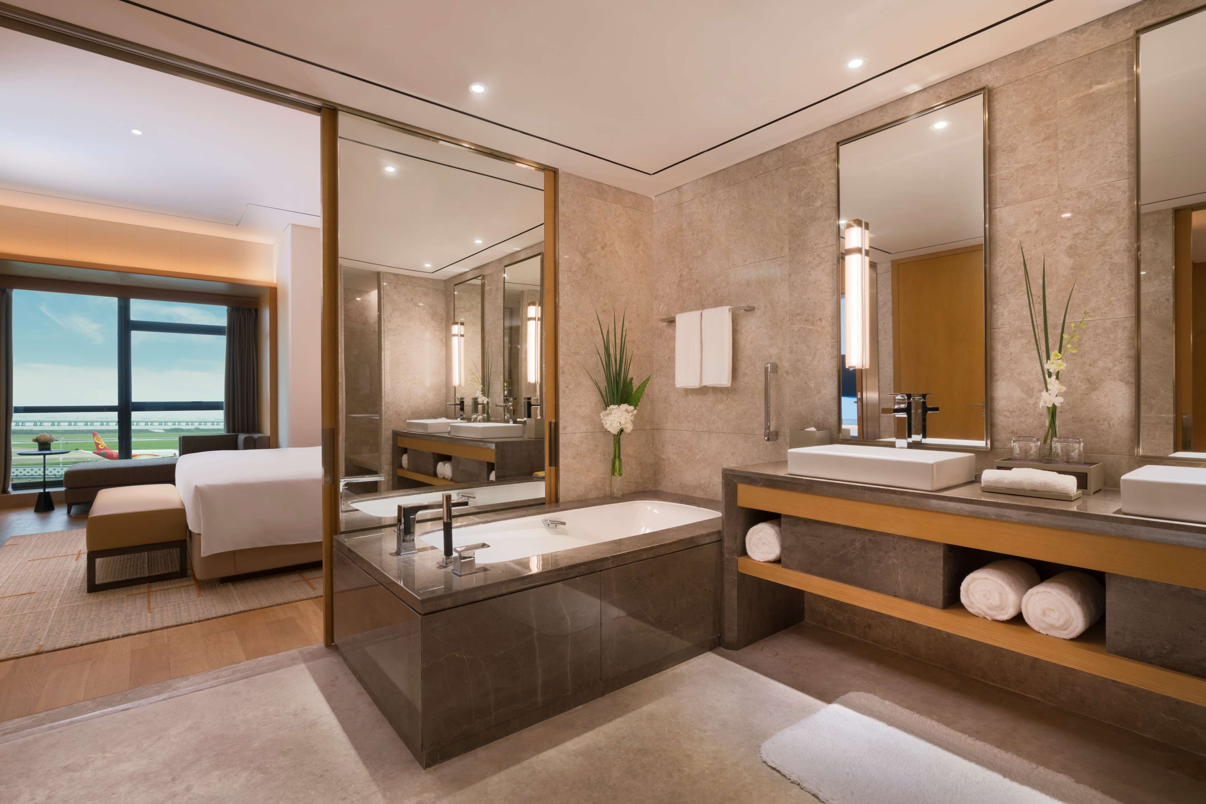A modern hotel bathroom with a large bathtub, two sinks, and a large mirror.
