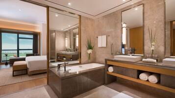 A modern hotel bathroom with a large bathtub, two sinks, and a large mirror.