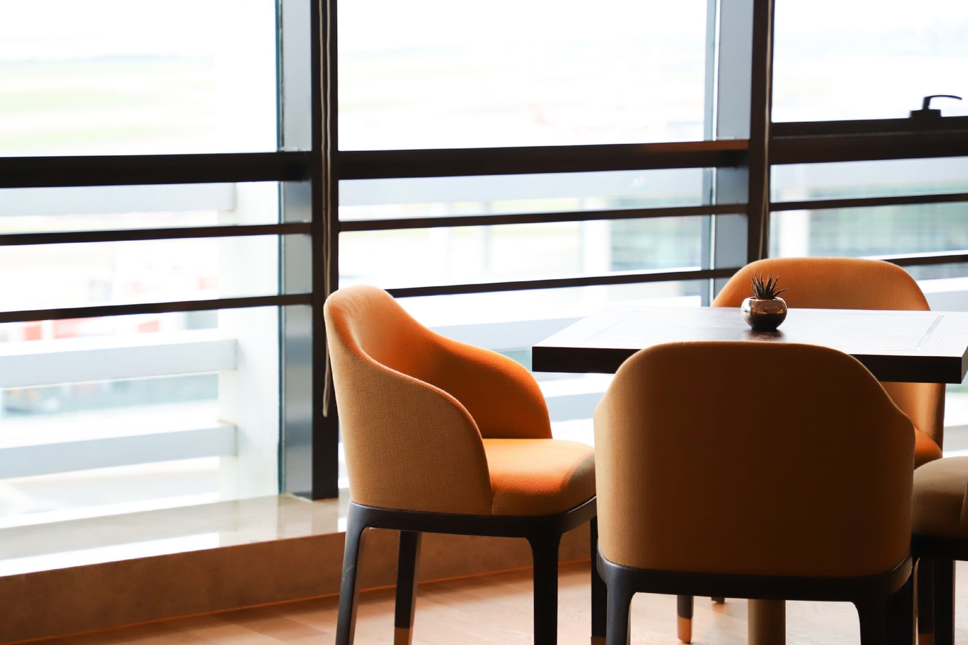 A modern interior with a large window, two orange chairs, and a table.