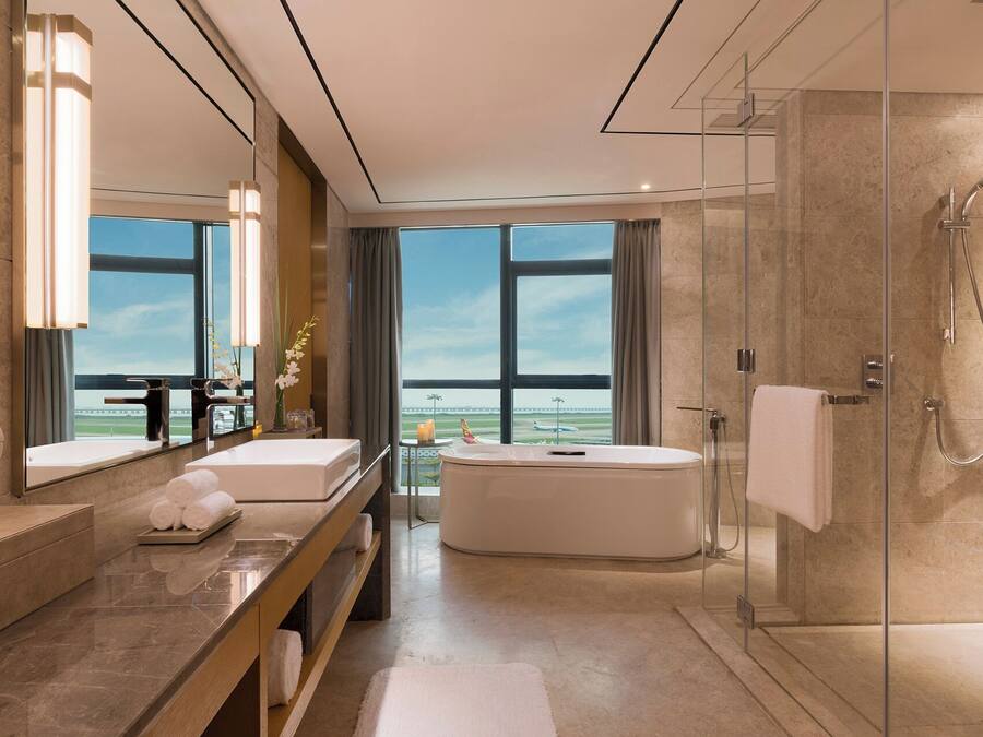 Un baño moderno con bañera, ducha y ventanas amplias que dan al aeropuerto.