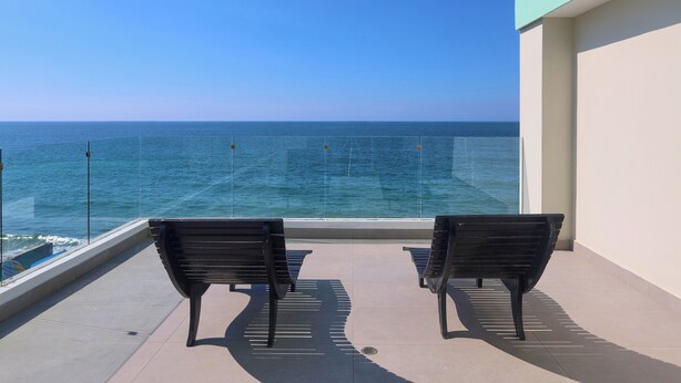 A balcony with two black benches facing a glass railing overlooking the sea. - Garner Hotel Mazatlan Beach by IHG (Mazatlán)
