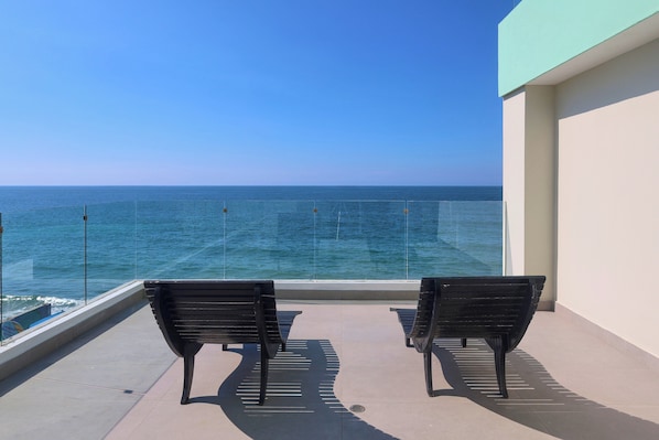 Un balcón con dos bancos negros frente a una barandilla de cristal con vistas al mar.