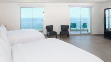 Habitación de hotel con una cama grande, dos sillones y un balcón con vista al mar.